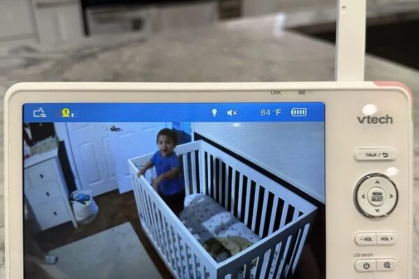 How Does VTech Baby Monitor Work? The Ultimate Guide! A VTech baby monitor displaying a live video feed of a young child standing inside a white crib. The monitor screen shows the room temperature, volume controls, and other settings. The background features a modern kitchen with a marble countertop. | How Does VTech Baby Monitor Work